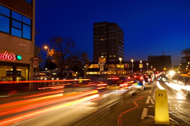 cars driving at night through a busy town centre with their headlights on